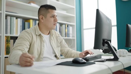 Téléchargez les photos : Jeune homme hispanique étudiant utilisant l'écriture informatique sur le document à l'université de la bibliothèque - en image libre de droit