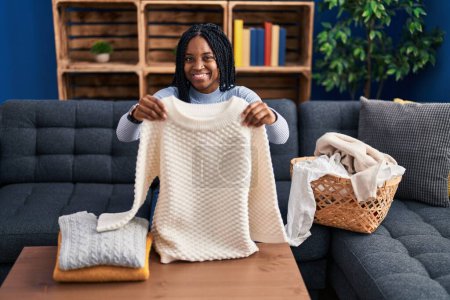 Photo for African american woman folding clean laundry winking looking at the camera with sexy expression, cheerful and happy face. - Royalty Free Image
