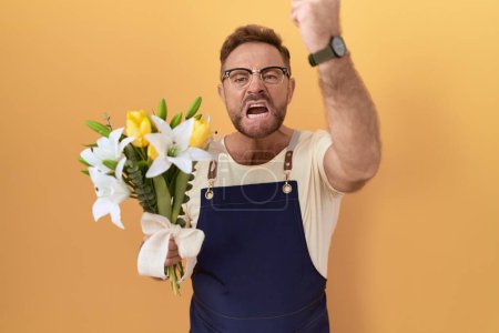 Photo for Middle age man with beard florist shop holding flowers angry and mad raising fist frustrated and furious while shouting with anger. rage and aggressive concept. - Royalty Free Image