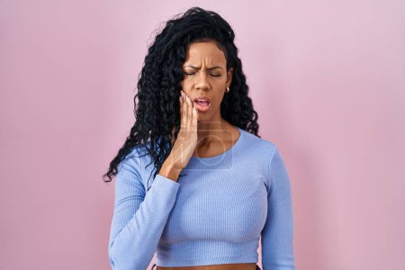 Foto de Mujer hispana de mediana edad de pie sobre fondo rosa tocando la boca con la mano con expresión dolorosa debido a dolor de muelas o enfermedad dental en los dientes. dentista - Imagen libre de derechos