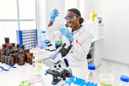 Foto de Científica afroamericana vertiendo líquido en tubo de ensayo en laboratorio - Imagen libre de derechos