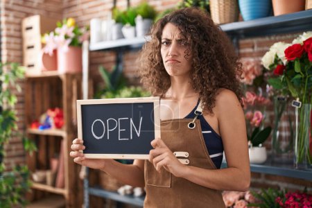 Photo for Hispanic woman with curly hair working at florist holding open sign skeptic and nervous, frowning upset because of problem. negative person. - Royalty Free Image