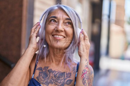 Photo for Middle age grey-haired woman smiling confident listening to music at street - Royalty Free Image