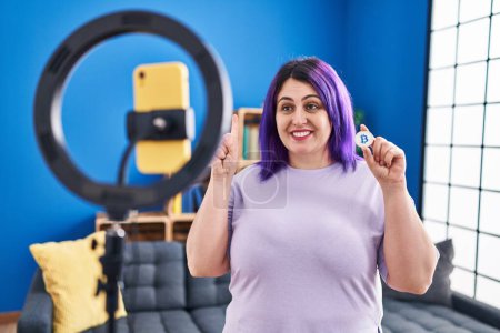 Téléchargez les photos : Plus taille femme avec cheveux violets enregistrement tutoriel Bitcoin avec smartphone à la maison souriant avec une idée ou une question pointant du doigt avec un visage heureux, numéro un - en image libre de droit