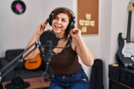 Foto de Mujer de mediana edad músico sonriendo con confianza cantando canción en el estudio de música - Imagen libre de derechos