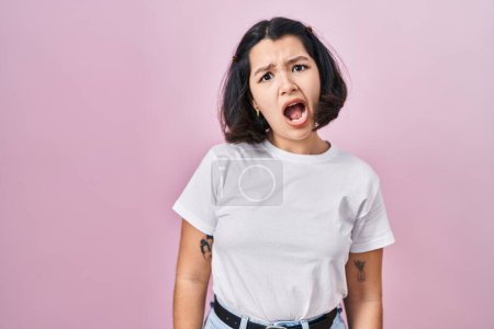 Téléchargez les photos : Jeune femme hispanique portant t-shirt blanc décontracté sur fond rose dans le visage de choc, l'air sceptique et sarcastique, surpris avec la bouche ouverte - en image libre de droit
