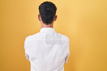 Foto de Joven hispano de pie sobre fondo amarillo mirando hacia atrás con los brazos cruzados - Imagen libre de derechos
