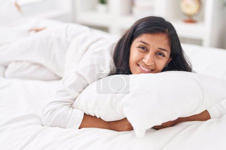 Foto de Joven hermosa mujer hispana abrazando almohada acostada en la cama en el dormitorio - Imagen libre de derechos
