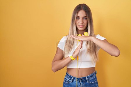 Téléchargez les photos : Jeune femme blonde debout sur fond jaune portant des écouteurs faisant un geste avec les mains, frustré et sérieux visage - en image libre de droit