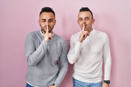 Téléchargez les photos : Couple homosexuel debout sur fond rose demandant à être calme avec le doigt sur les lèvres. silence et concept secret. - en image libre de droit