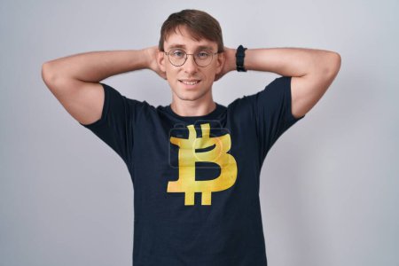 Photo for Caucasian blond man wearing bitcoin t shirt relaxing and stretching, arms and hands behind head and neck smiling happy - Royalty Free Image