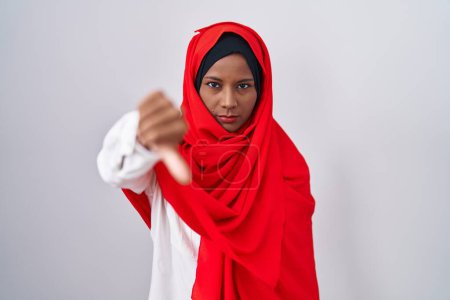 Photo for Young arab woman wearing traditional islamic hijab scarf looking unhappy and angry showing rejection and negative with thumbs down gesture. bad expression. - Royalty Free Image