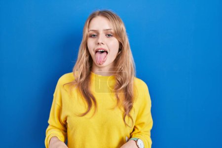 Téléchargez les photos : Jeune femme caucasienne debout sur fond bleu langue collante heureux avec une expression drôle. concept d'émotion. - en image libre de droit