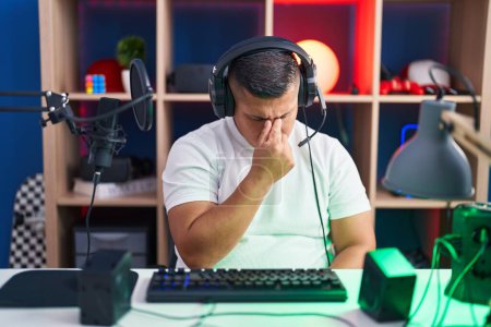 Photo for Young hispanic man playing video games tired rubbing nose and eyes feeling fatigue and headache. stress and frustration concept. - Royalty Free Image
