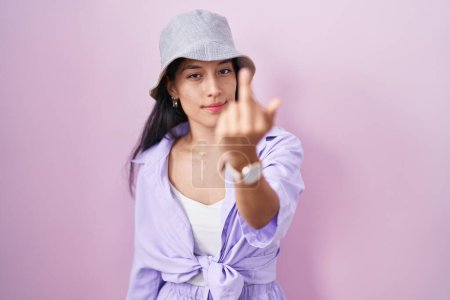Photo for Young hispanic woman standing over pink background wearing hat showing middle finger, impolite and rude fuck off expression - Royalty Free Image