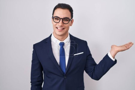 Photo for Young hispanic man wearing suit and tie smiling cheerful presenting and pointing with palm of hand looking at the camera. - Royalty Free Image