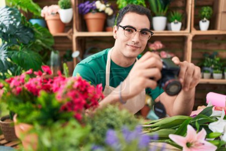 Téléchargez les photos : Jeune homme hispanique fleuriste tenant caméra professionnelle à la boutique de fleurs - en image libre de droit