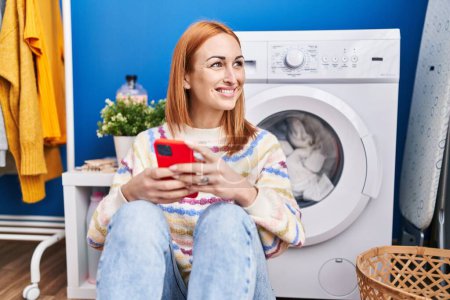 Photo for Young caucasian woman using smartphone waiting for washing machine at laundry room - Royalty Free Image