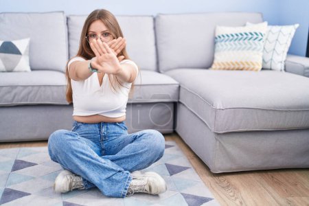 Photo for Young caucasian woman sitting on the floor at the living room rejection expression crossing arms and palms doing negative sign, angry face - Royalty Free Image