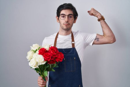 Téléchargez les photos : Jeune homme hispanique tenant bouquet de roses blanches et rouges personne forte montrant muscle du bras, confiant et fier de la puissance - en image libre de droit
