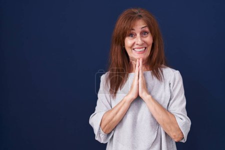 Photo for Middle age woman standing over blue background praying with hands together asking for forgiveness smiling confident. - Royalty Free Image