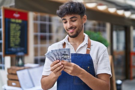 Foto de Joven árabe camarero contando dólares trabajando en restaurante - Imagen libre de derechos