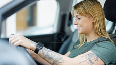 Téléchargez les photos : Jeune femme blonde souriant voiture de conduite confiante à la rue - en image libre de droit