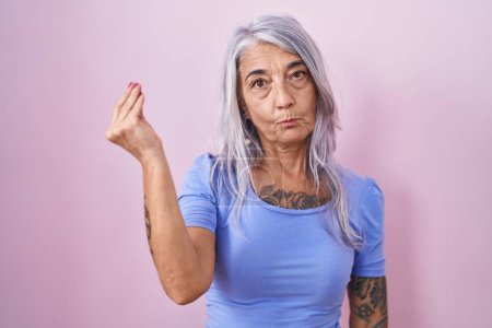 Téléchargez les photos : Femme d'âge moyen avec des tatouages debout sur fond rose faisant geste italien avec la main et les doigts expression confiante - en image libre de droit