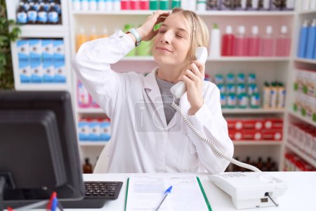 Téléchargez les photos : Jeune femme caucasienne travaillant à la pharmacie pharmacie parlant au téléphone souriant confiant toucher les cheveux avec geste de la main vers le haut, posant attrayant et à la mode - en image libre de droit