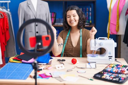 Photo for Young hispanic tailor woman doing tutorial with smartphone screaming proud, celebrating victory and success very excited with raised arm - Royalty Free Image