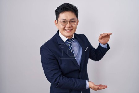 Téléchargez les photos : Jeune homme asiatique portant costume d'affaires et cravate geste avec les mains montrant grand et grand signe de taille, symbole de mesure. souriant en regardant la caméra. concept de mesure. - en image libre de droit