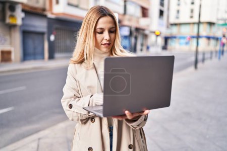 Photo for Young blonde woman using laptop standing at street - Royalty Free Image