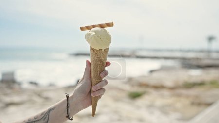 Téléchargez les photos : Jeune femme blonde tenant de la crème glacée à la plage - en image libre de droit