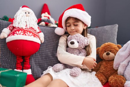 Téléchargez les photos : Adorable fille hispanique étreignant ours en peluche assis sur le canapé par la décoration de Noël à la maison - en image libre de droit