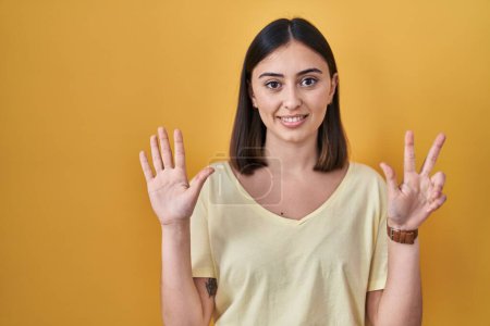 Photo for Hispanic girl wearing casual t shirt over yellow background showing and pointing up with fingers number eight while smiling confident and happy. - Royalty Free Image