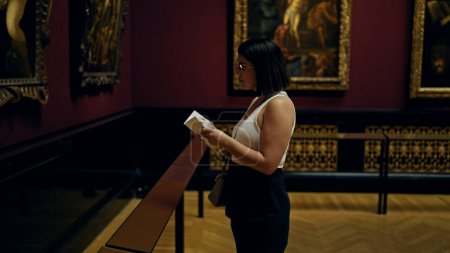 Photo for Young beautiful hispanic woman visiting art gallery reading brochure at Art Museum in Vienna - Royalty Free Image