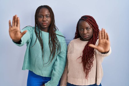 Photo for Two african woman standing over blue background doing stop sing with palm of the hand. warning expression with negative and serious gesture on the face. - Royalty Free Image