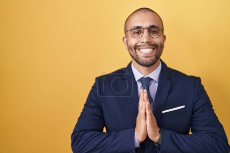 Photo for Hispanic man with beard wearing suit and tie praying with hands together asking for forgiveness smiling confident. - Royalty Free Image