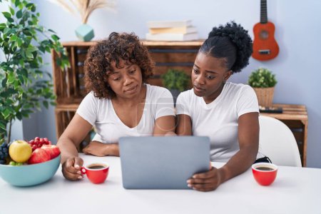 Photo for African american women mother and daughter drinking coffee using laptop at home - Royalty Free Image