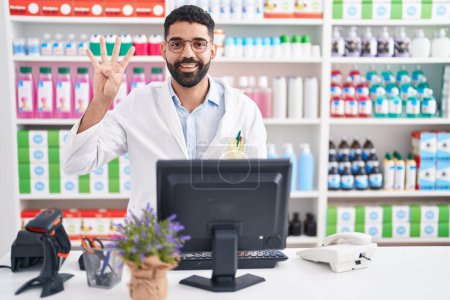 Photo for Hispanic man with beard working at pharmacy drugstore showing and pointing up with fingers number four while smiling confident and happy. - Royalty Free Image