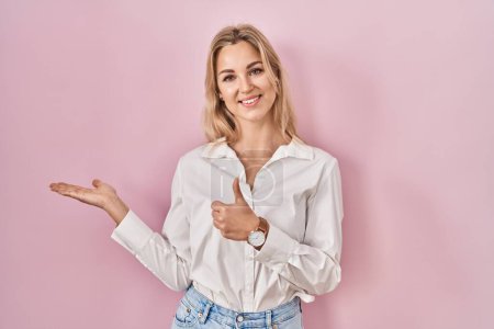 Téléchargez les photos : Jeune femme caucasienne portant une chemise blanche décontractée sur fond rose montrant la main de la paume et faisant un geste correct avec les pouces levés, souriant heureux et joyeux - en image libre de droit