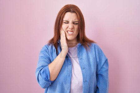 Téléchargez les photos : Jeune femme hispanique aux cheveux roux debout sur fond rose touchant la bouche avec la main avec une expression douloureuse à cause de maux de dents ou de maladies dentaires sur les dents. dentiste - en image libre de droit
