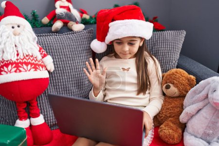 Photo for Adorable hispanic girl wearing christmas hat having video call at home - Royalty Free Image