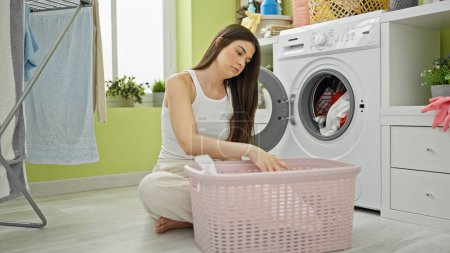 Téléchargez les photos : Jeune belle femme hispanique laver les vêtements fatigué à la buanderie - en image libre de droit