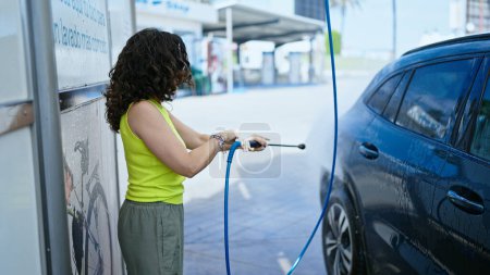 Photo for Middle age hispanic woman washing car with pressure washer at car wash station - Royalty Free Image