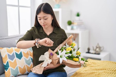 Téléchargez les photos : Jeune femme chinoise tenant bouquet de fleurs blanches vérifiant l'heure sur la montre-bracelet, détendu et confiant - en image libre de droit