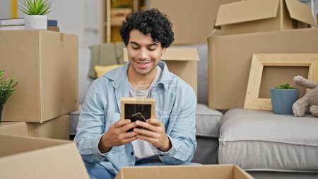 Photo for Young latin man packing cardboard box looking photo at new home - Royalty Free Image
