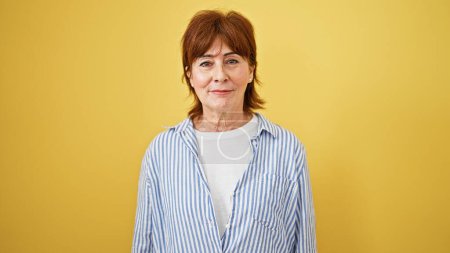 Téléchargez les photos : Femme d'âge moyen debout avec une expression sérieuse sur fond jaune isolé - en image libre de droit