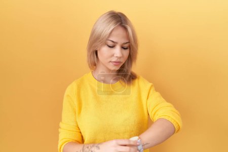 Photo for Young caucasian woman wearing yellow sweater checking the time on wrist watch, relaxed and confident - Royalty Free Image