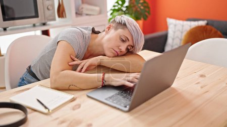 Téléchargez les photos : Jeune femme fatiguée en utilisant un ordinateur portable à la salle à manger - en image libre de droit